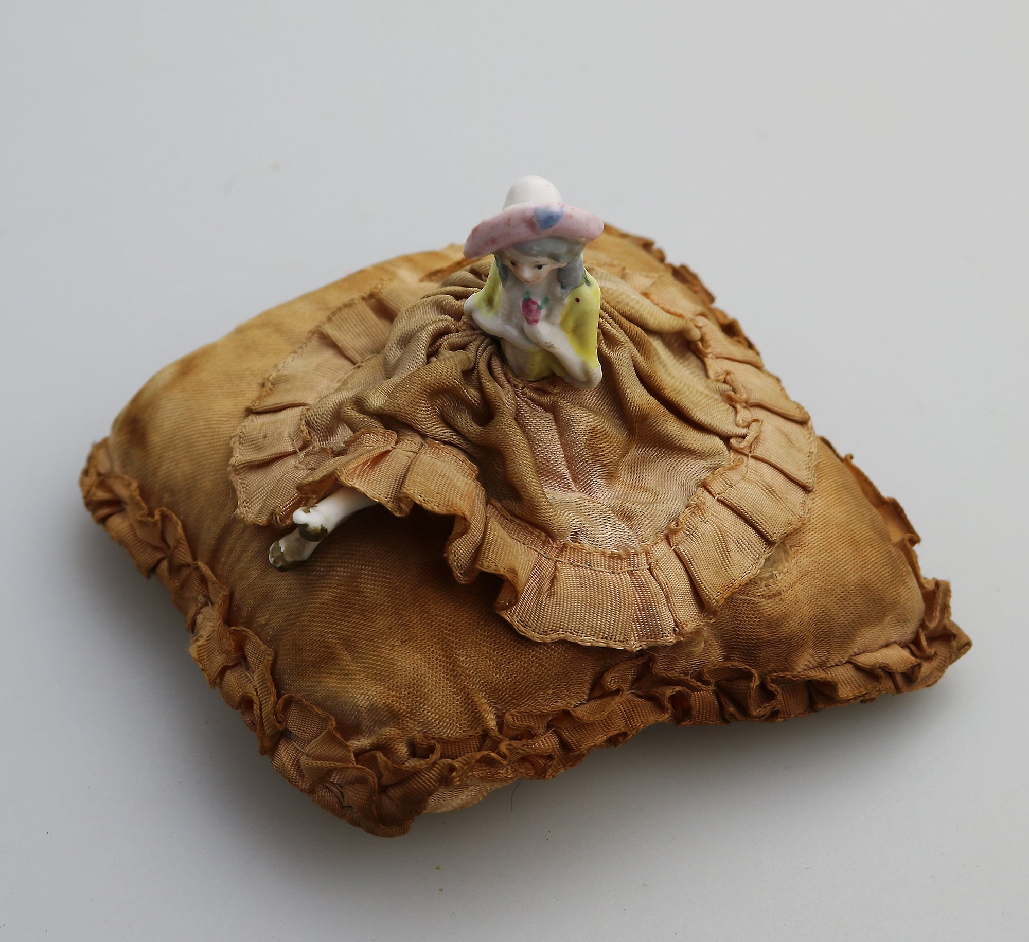 A good antique hand-painted porcelain half doll with legs on cushion C.early 20thC
